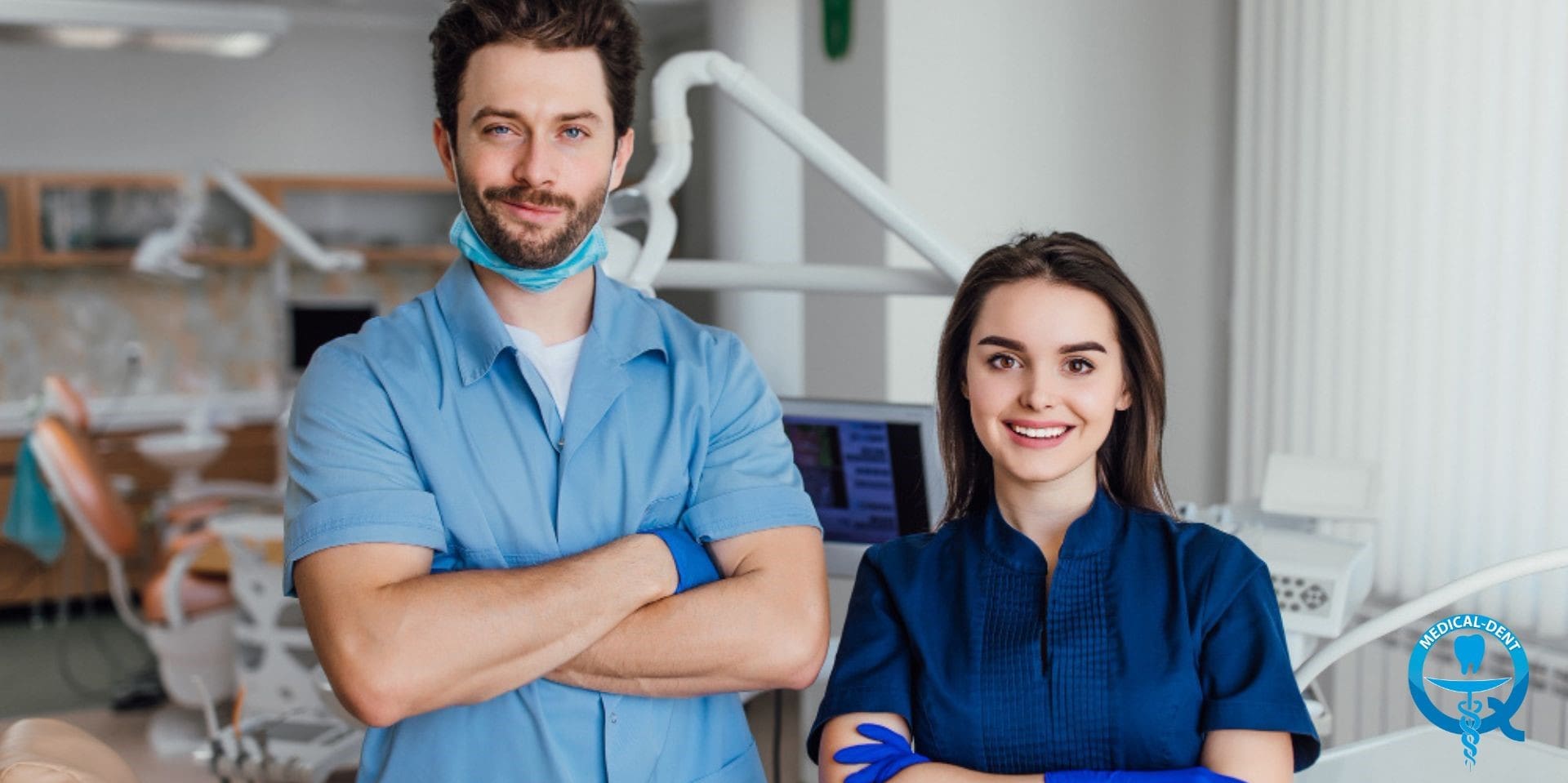 The image shows two smiling dentists working in a dental practice in the UK. The man is wearing a blue shirt and medical mask and the woman is dressed in a navy blue blouse. Behind them, dental equipment and the practice's logo can be seen.