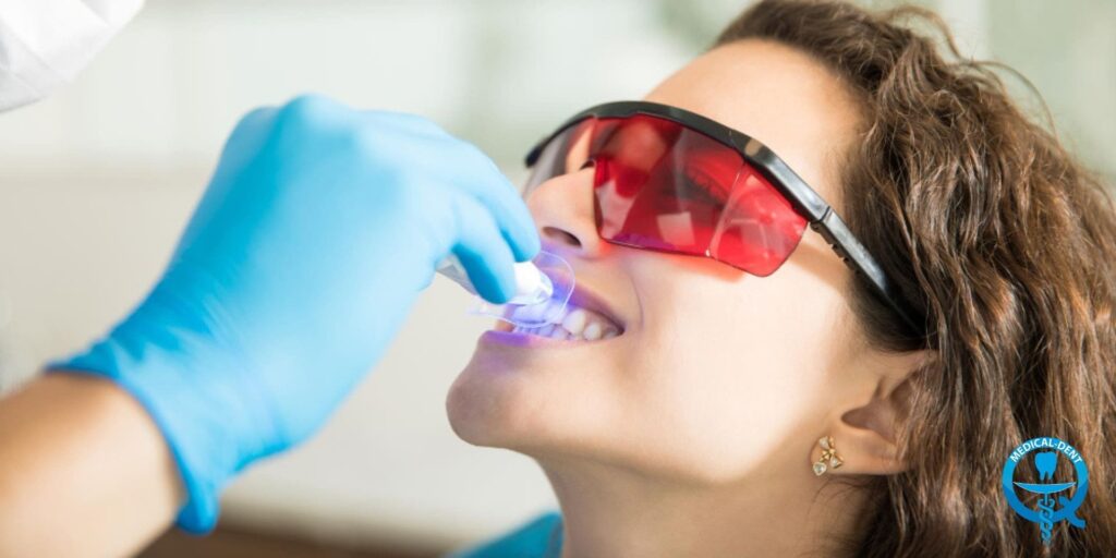 The image shows a masked patient during a cosmetic dental procedure. We see a close-up of the face of a person wearing red safety goggles, with a blue polymerisation lamp used to cure fillings zooming in on their mouth. This is an illustration of a cosmetic dentistry procedure.